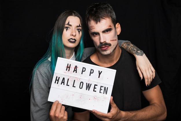 Foto gratuita jóvenes amigos con maquillaje de halloween con letrero