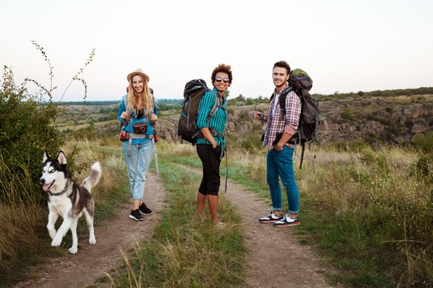 Jóvenes amigos con mochilas y huskies sonriendo, viajando en el cañón