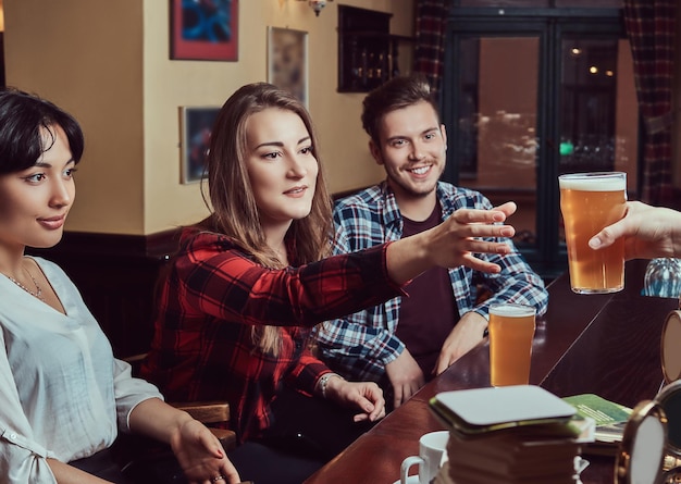 Jóvenes amigos multirraciales en el bar. barman dando un vaso de cerveza al cliente en el pub.