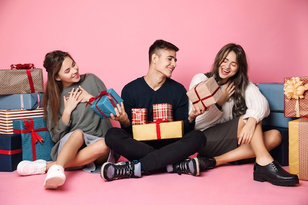 Jóvenes amigos sentados entre cajas de regalo de navidad en rosa