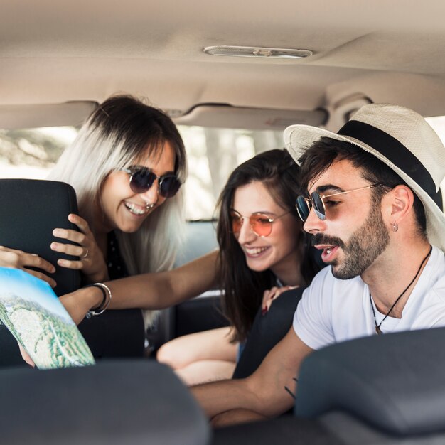 Jóvenes amigos sentados dentro del coche moderno mirando el mapa