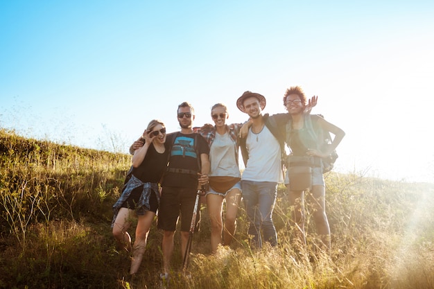 Jóvenes amigos sonriendo, regocijándose, de pie en el campo