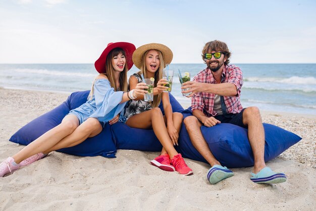 Jóvenes amigos sonrientes de vacaciones sentados en bolsas de frijoles en una fiesta en la playa