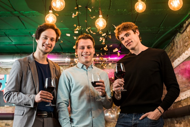 Jóvenes amigos varones con copas de vino disfrutando en la fiesta en el bar