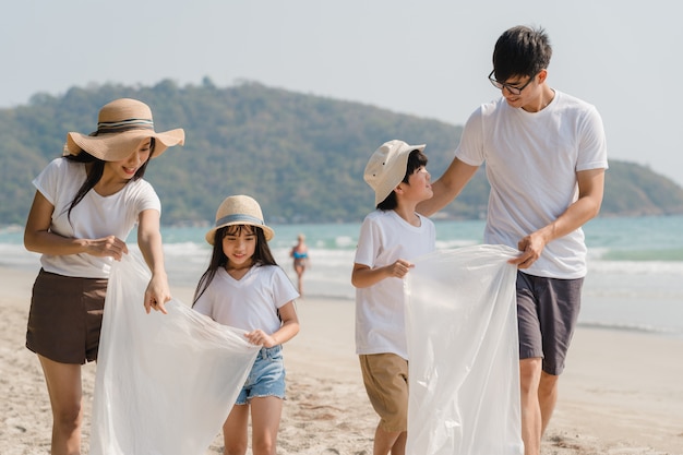 Jóvenes asiáticos felices activistas familiares recogiendo residuos plásticos y caminando en la playa. Los voluntarios de Asia ayudan a mantener la naturaleza limpia de basura. Concepto sobre problemas de contaminación de conservación ambiental.