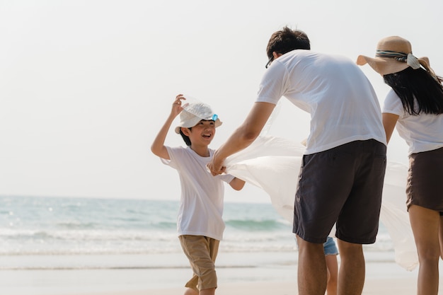 Jóvenes asiáticos felices activistas familiares recogiendo residuos plásticos en la playa. Los voluntarios de Asia ayudan a mantener la naturaleza limpia y recoger la basura. Concepto sobre problemas de contaminación de conservación ambiental.