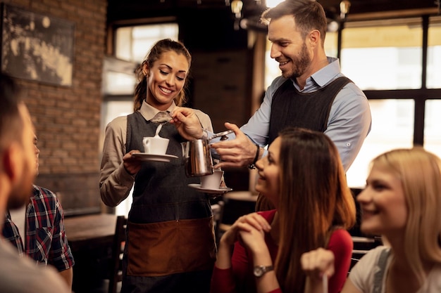 Foto gratuita jóvenes camareros felices cooperando mientras atienden a sus invitados y agregan crema de leche mientras preparan café