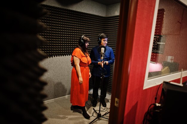 Jóvenes cantantes asiáticos de dúo con micrófono grabando una canción en un estudio de grabación de música