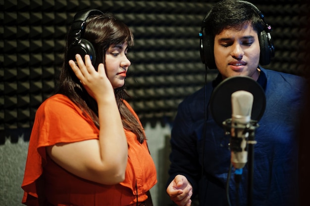 Jóvenes cantantes asiáticos de dúo con micrófono grabando una canción en un estudio de grabación de música