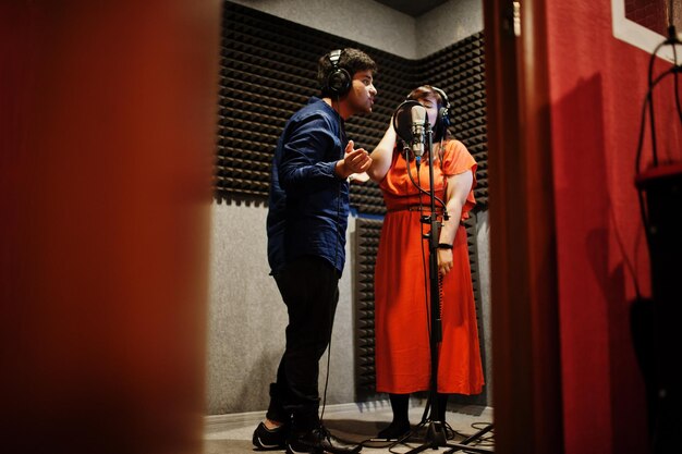 Jóvenes cantantes asiáticos de dúo con micrófono grabando una canción en un estudio de grabación de música