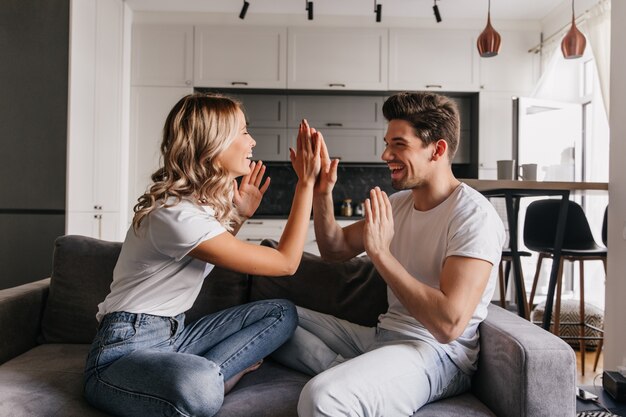 Jóvenes caucásicos posando en elegante piso. Retrato interior de una pareja despreocupada sonriendo en el sofá.