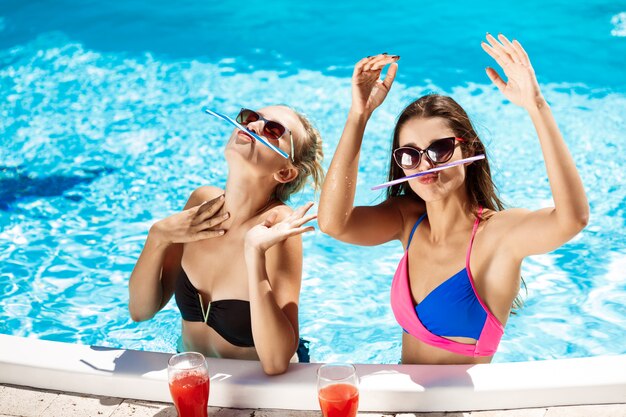 Jóvenes chicas guapas sonriendo, engañando, hablando, relajándose en la piscina.