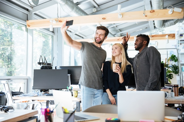 Jóvenes colegas alegres en coworking de oficina hacen selfie