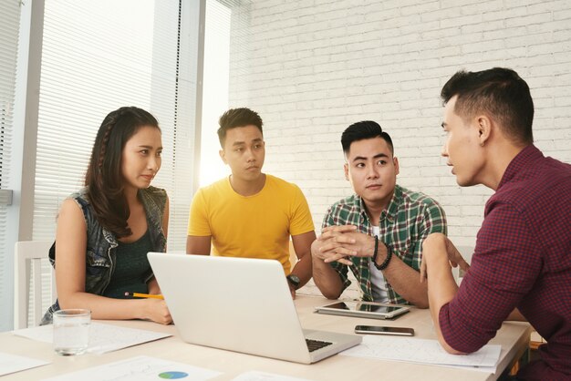 Jóvenes colegas asiáticos vestidos casualmente, intercambiando ideas en la oficina