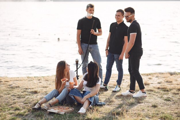 Jóvenes comiendo pizza y fumando shisha en la playa