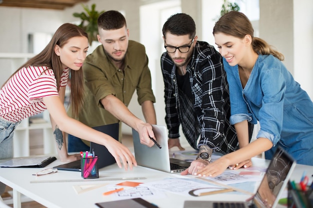 Jóvenes creativos que trabajan juntos con una computadora portátil Grupo de chicos geniales que trabajan en un nuevo proyecto mientras pasan tiempo en una oficina moderna