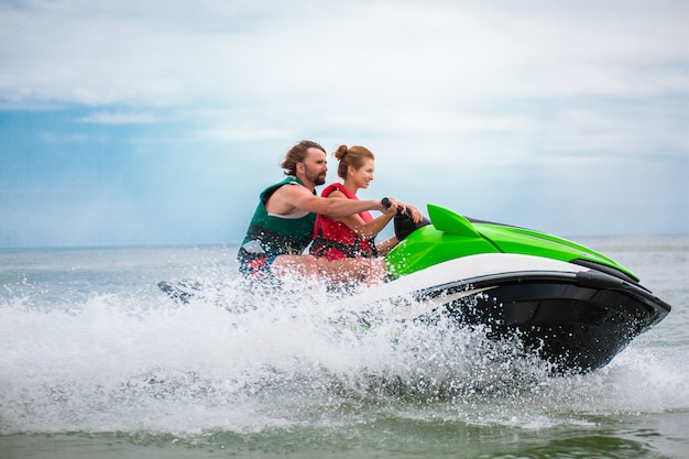 Los jóvenes se divierten conduciendo a alta velocidad en motos de agua, hombre y mujer en vacaciones de verano, amigos haciendo deporte activo