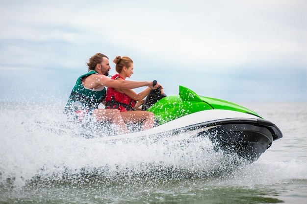 Los jóvenes se divierten conduciendo a alta velocidad en motos de agua, hombre y mujer en vacaciones de verano, amigos haciendo deporte activo