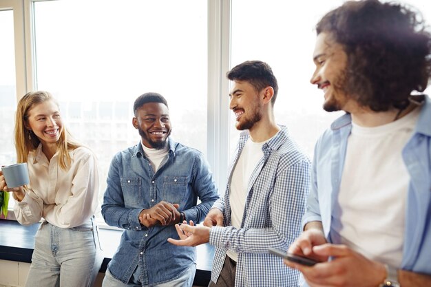 Los jóvenes empresarios alegres tienen una charla durante la pausa para el café en la oficina