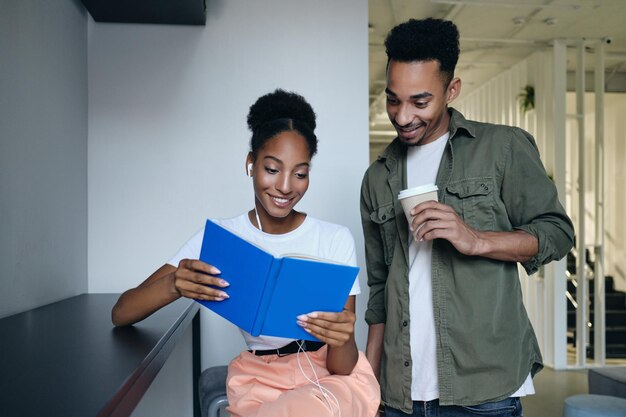 Jóvenes estudiantes afroamericanos casuales felizmente leyendo libros juntos en un moderno espacio de trabajo conjunto