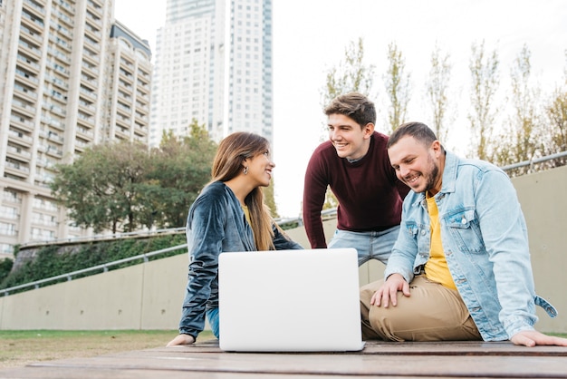 Foto gratuita jóvenes estudiantes independientes trabajando en una computadora portátil afuera.