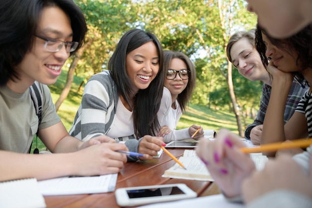 Jóvenes estudiantes sentados y estudiando al aire libre mientras hablan