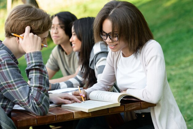 Jóvenes estudiantes sentados y estudiando al aire libre mientras hablan