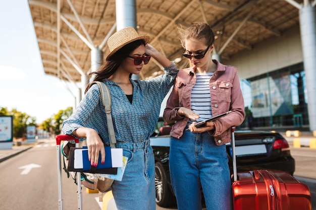 Jóvenes hermosas chicas alegres sosteniendo cócteles en las manos mirando felizmente a la cámara mientras pasan tiempo juntas en el viejo y acogedor patio de la cafetería