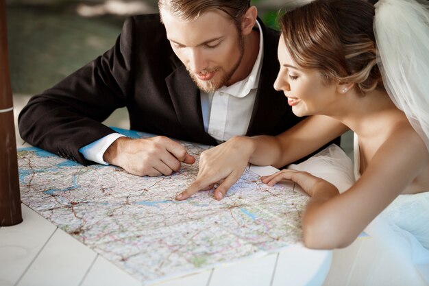 Jóvenes hermosos recién casados sonriendo, elegir viaje de luna de miel, mirando el mapa.