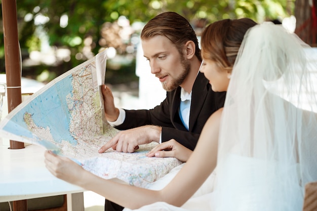 Jóvenes hermosos recién casados sonriendo, elegir viaje de luna de miel, mirando el mapa.