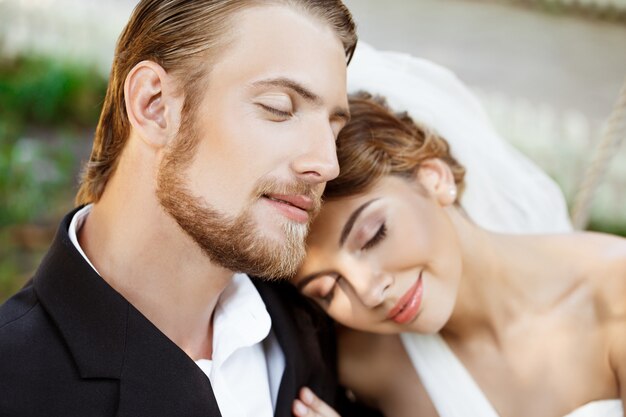 Jóvenes hermosos recién casados sonriendo con los ojos cerrados, disfrutando.