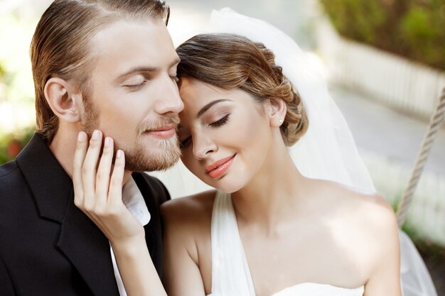 Jóvenes hermosos recién casados sonriendo con los ojos cerrados, disfrutando.