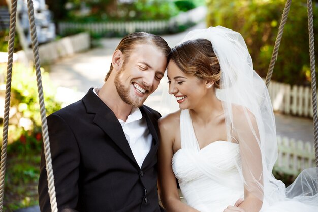 Jóvenes hermosos recién casados sonriendo, riendo, sentado en el columpio en el parque.