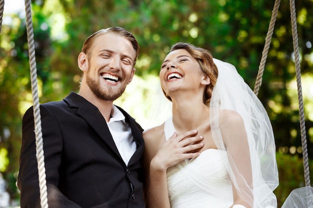 Jóvenes hermosos recién casados sonriendo, riendo, sentado en el columpio en el parque.