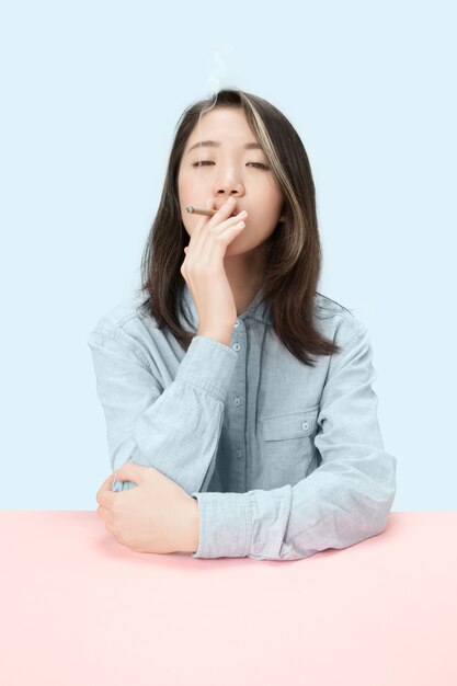 Jóvenes mujeres coreanas fumando puros mientras están sentados a la mesa en el estudio. Colores de moda