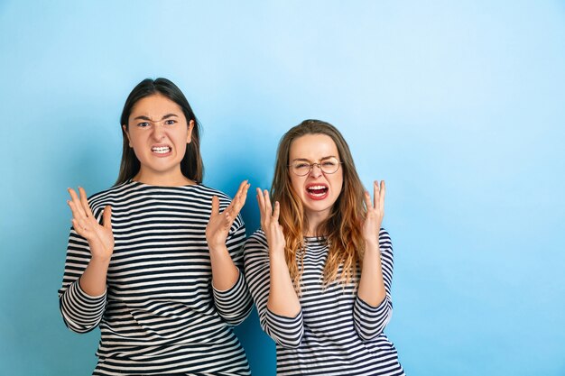 Jóvenes mujeres emocionales aisladas en la pared del estudio azul degradado