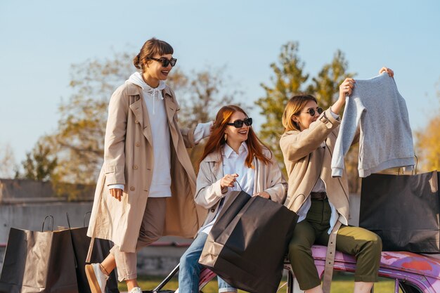 Jóvenes mujeres felices con bolsas de compras posando cerca de un viejo coche decorado