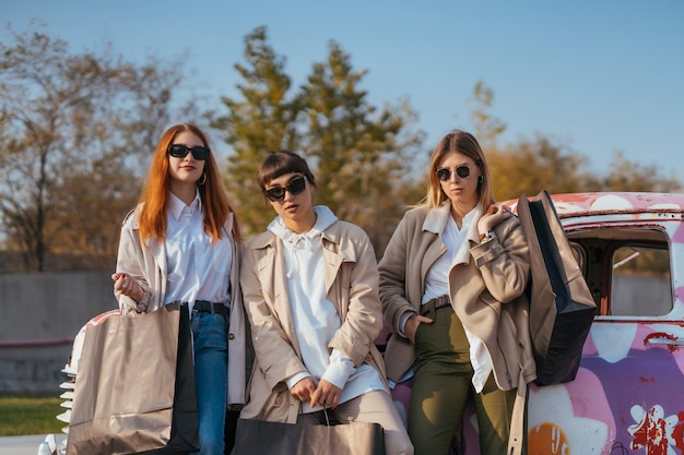 Jóvenes mujeres felices con bolsas de compras posando cerca de un viejo coche decorado