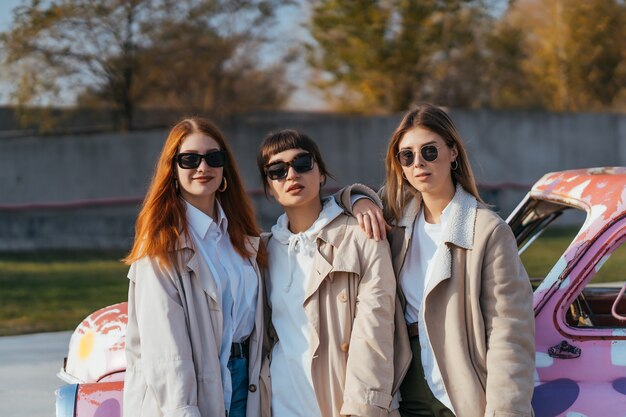 Jóvenes mujeres felices con bolsas de compras posando cerca de un viejo coche decorado