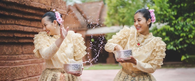 Foto gratuita jóvenes mujeres sonrientes se visten con hermosos trajes tailandeses salpicando agua en los templos y preservan la buena cultura de los tailandeses durante el festival songkran, día de la familia del año nuevo tailandés en abril