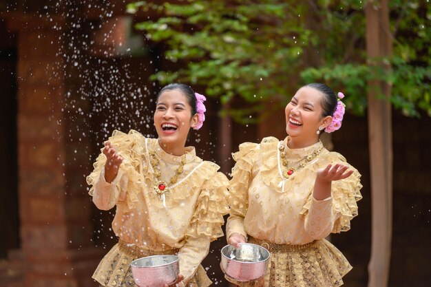 Jóvenes mujeres sonrientes se visten con hermosos trajes tailandeses salpicando agua en los templos y preservan la buena cultura de los tailandeses durante el festival Songkran, Día de la Familia del Año Nuevo Tailandés en abril