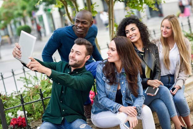 Jóvenes multiétnicos tomando selfie juntos en backgr urbana