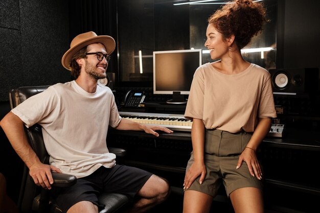 Jóvenes músicos con estilo mirándose felizmente trabajando juntos en un moderno estudio de grabación de sonido