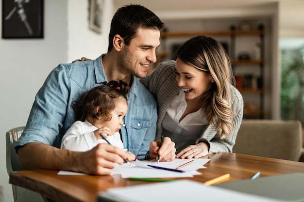 Jóvenes padres felices disfrutando coloreando con su pequeña hija en casa