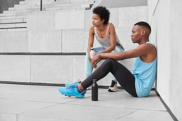 Los jóvenes pensativos tienen una forma de cuerpo deportivo, motivación para estar sanos y en forma, hacer deporte al aire libre, subir escaleras, tomar un descanso para beber agua y refrescarse, ser fuerte. Concepto de fitness