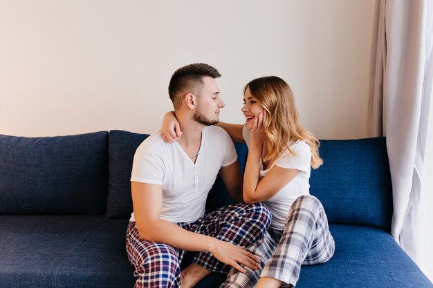 Jóvenes en pijama lindo mirando el uno al otro. Hermosa chica rubia en pantalones a cuadros abrazando a su novio.