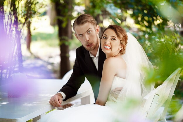 Jóvenes recién casados hermosos engañando, sentado en la cafetería al aire libre.