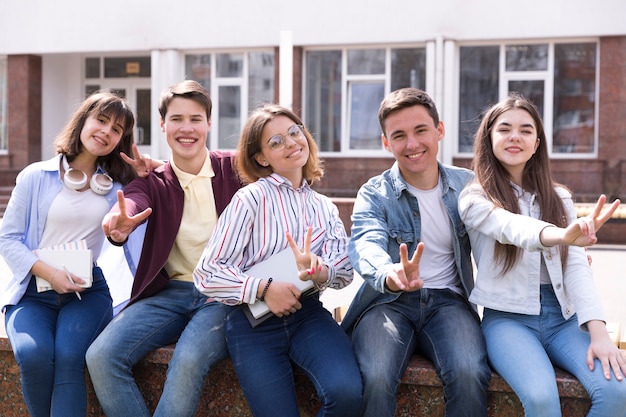 Jóvenes sentados con libros y gesticulando dos dedos.