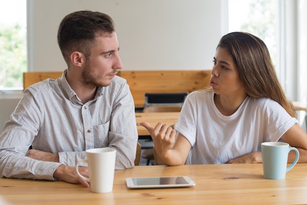 Jóvenes serios charlando y tomando té en la cafetería