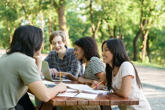 Jóvenes sonrientes estudiantes sentados y estudiando al aire libre